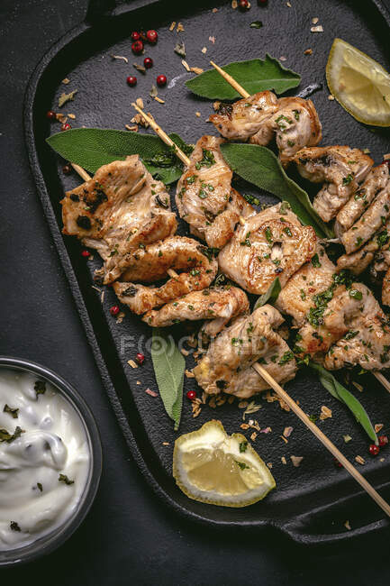 From above of appetizing freshly cooked meat on skewers served on tray on black table with bowl of sauce — Stock Photo