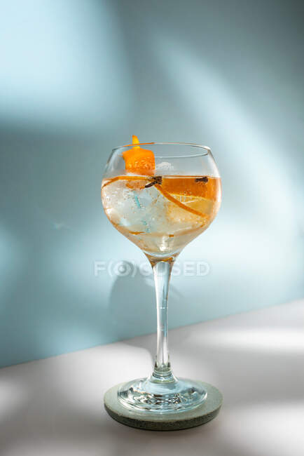 Transparent glass of highball cocktail decorated with citrus fruit zest and clove against shadows in sunlight — Stock Photo