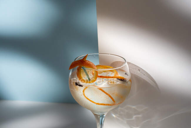 Transparent glass of highball cocktail decorated with citrus fruit zest and clove against shadows in sunlight — Stock Photo