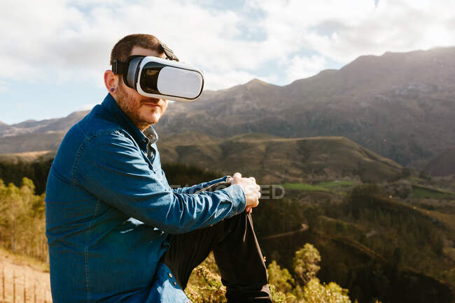 Цікавий чоловік - мандрівник сидить на пагорбі і в сонячний день відчуває віртуальну реальність в окулярах у горах. — стокове фото