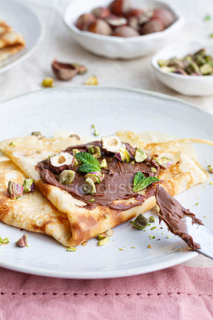 Delicious crepes garnished with chocolate and nuts served on plate on table for breakfast — Stock Photo