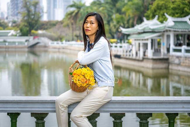 Beautiful Asian's girl portrait in a park while she sits next to wicker basket with yellow flowers. — Stock Photo