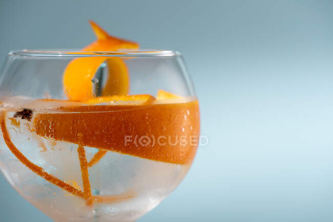 Bicchiere trasparente di cocktail highball decorato con scorza di agrumi e chiodi di garofano contro le ombre alla luce del sole — Foto stock
