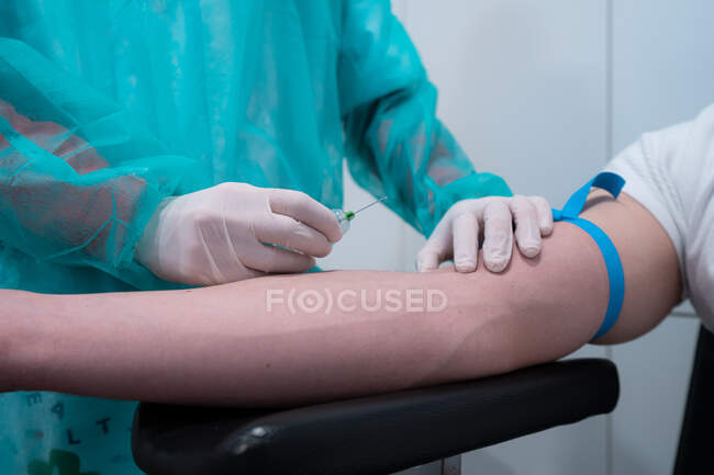 Crop unrecognizable medic with needle and syringe collecting blood from vein of patient in hospital — Stock Photo
