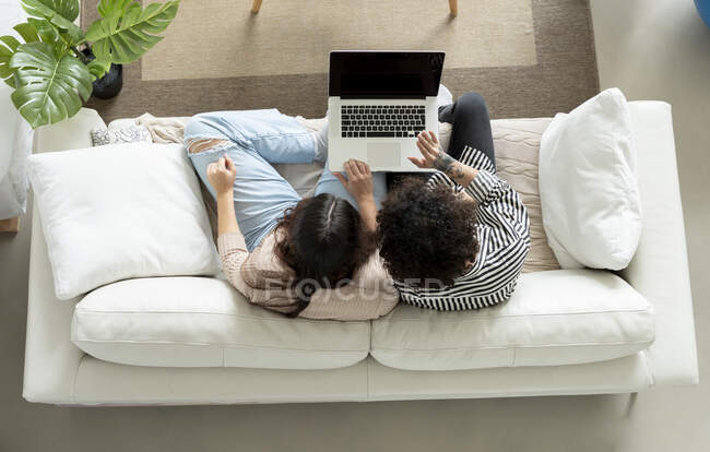 De arriba la pareja que navega el portátil en el sofá en la habitación de casa - foto de stock