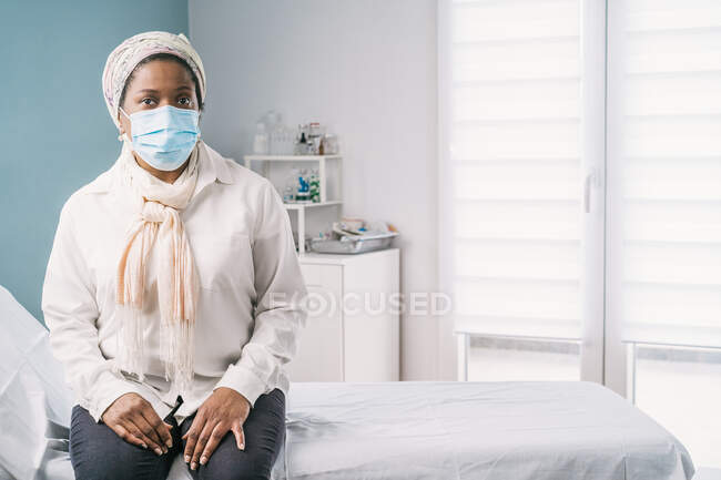 Afro-americano paziente donna matura con maschera facciale seduto al letto clinica in attesa di appuntamento durante l'appuntamento durante l'epidemia di coronavirus — Foto stock