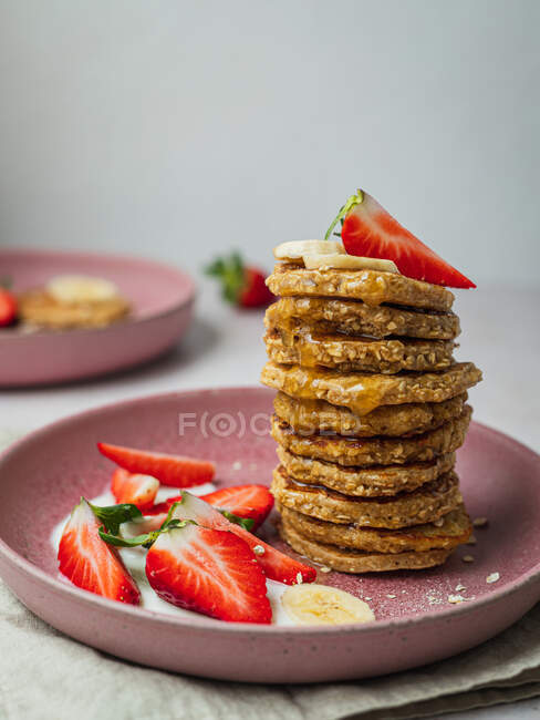 Plate with a row of banana pancakes and a few pieces of strawberries — Stock Photo