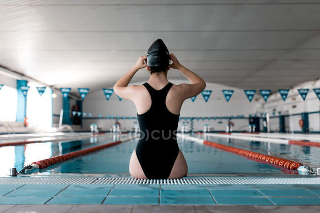 Schwimmer sitzt am Beckenrand und setzt seine Schwimmbrille auf — Stockfoto