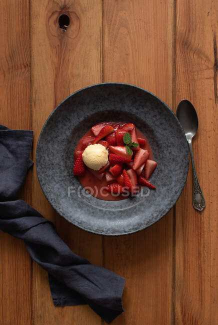 Draufsicht auf leckere Erdbeerhälften mit Vanilleeis im Teller auf Holztisch — Stockfoto