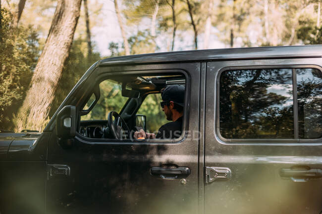 Side view of an adventurer using his smartphone inside his off-road car before starting the journey — Stock Photo