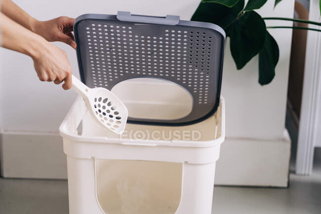 Crop unrecognizable person with plastic shovel opening lid of pet toilet box in house room — Stock Photo