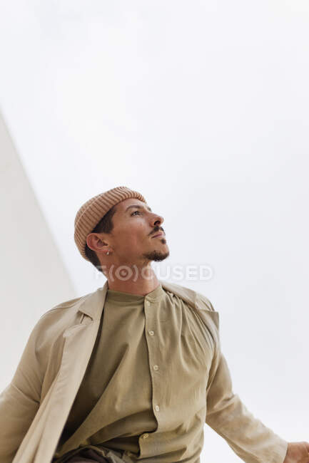 Serious male wearing trendy coat and hat standing in city and looking away — Stock Photo