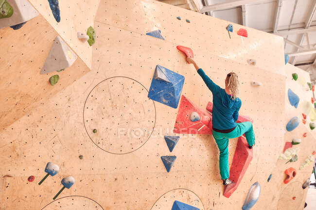 Vista posteriore a basso angolo di anonima parete artificiale di arrampicata atletica femminile durante l'allenamento di boulder in palestra professionale — Foto stock