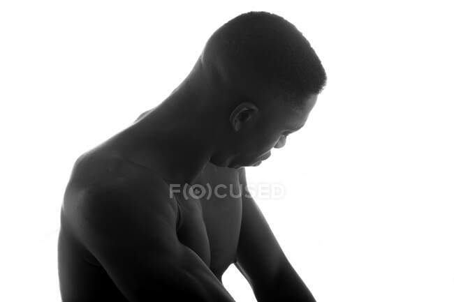 Negro y blanco de hombre negro musculoso sin camisa sin emociones mirando hacia abajo en el estudio sobre fondo blanco - foto de stock
