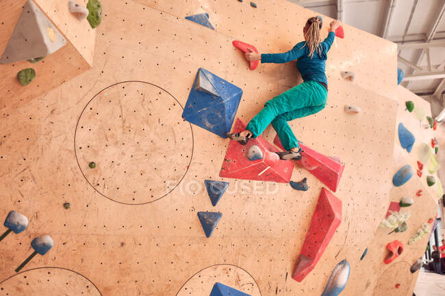 Low angle back view of anonymous female athlete climbing artificial wall during bouldering workout in professional gym — Stock Photo