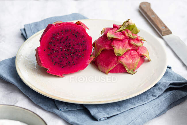 Pitaya saboroso brilhante com polpa suculenta e pequenas sementes na chapa cerâmica perto da faca na mesa — Fotografia de Stock