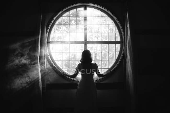 Back view of unrecognizable gentle female touching fence on round shaped window in house in sunlight — Stock Photo