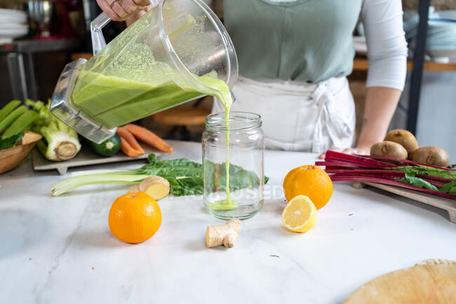 Анонимная самка урожая наливает вкусный смузи из блендера в банку за столом с цитрусовыми фруктами дома — стоковое фото