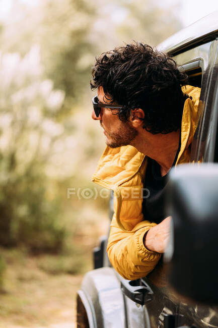Vista laterale di un avventuriero con occhiali da sole che sbircia fuori dalla vendita di auto con sfondo sfocato — Foto stock