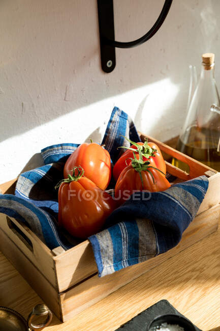 Grand angle de tomates rouges fraîches mûres placées sur un plateau en bois naturel avec serviette dans la cuisine de la maison — Photo de stock