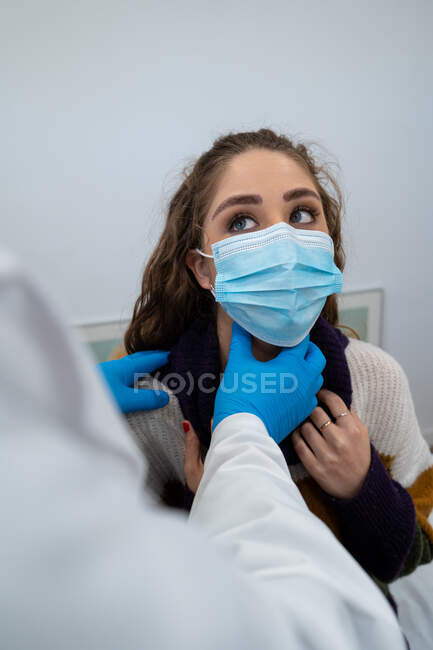 Médico irreconocible en guantes que examinan los ganglios linfáticos de la paciente durante la cita en el hospital moderno - foto de stock