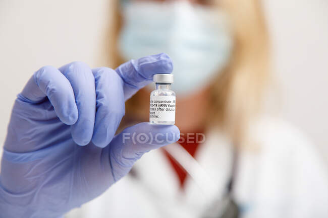 Medico femminile in maschera protettiva per il viso e guanti in lattice con flaconcino di vaccino coronavirus che mostra alla telecamera mentre in piedi in camera d'ospedale — Foto stock