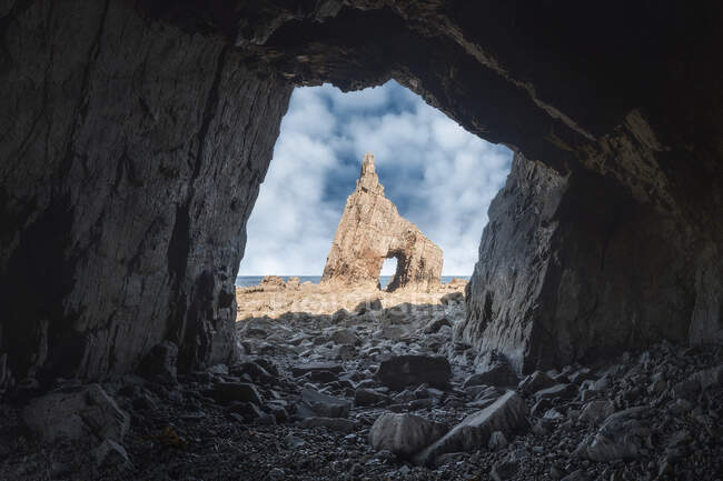 Грубый пещерный пейзаж острой скалы с отверстием на каменистом пляже Campiecho под голубым небом в Астурии — стоковое фото