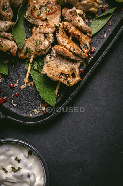 Зверху апетитне м'ясо на шампурах, подане на підносі на чорному столі з мискою соусу — стокове фото