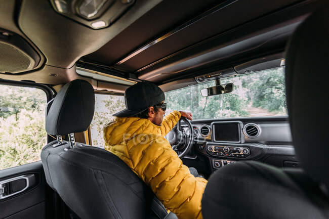 From behind inside view of a driver wearing a cap and sunglasses in an off-road car looking away — Stock Photo