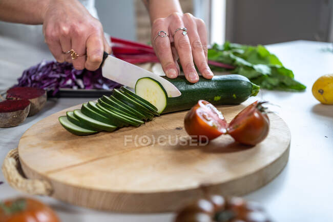 Corte abobrinha fêmea irreconhecível com faca enquanto prepara o almoço na mesa da cozinha em casa — Fotografia de Stock