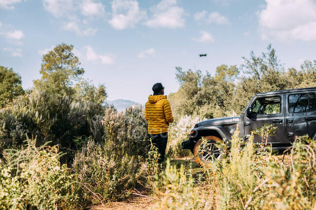 View from behind of an adventurer flying his drone next to his off-road car on the mountain — Stock Photo