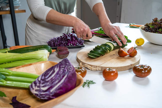 Crop unrecognizable female cutting zucchini with knife while preparing lunch at kitchen table in house — Stock Photo