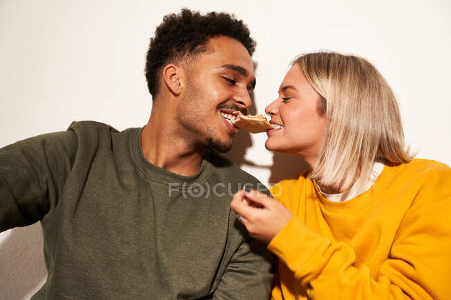 Positivo multirracial casal comer pizza fatia juntos enquanto se divertindo e olhando para o outro — Fotografia de Stock