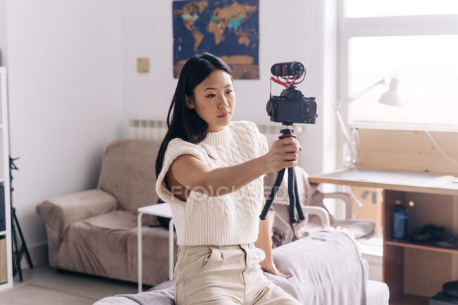 Серьёзные этнические женщины-блоггеры записывают видео на фотокамеру, стоя в гостиной — стоковое фото