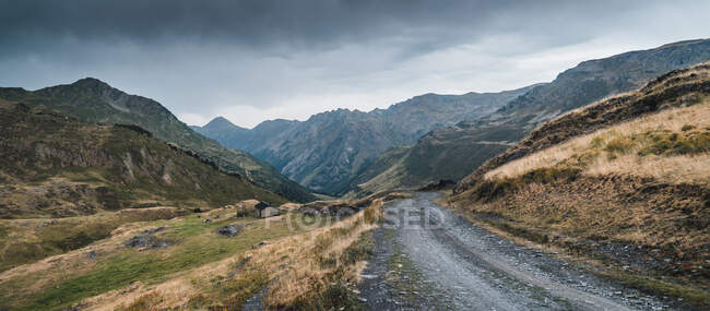 Paysage pittoresque de route vide entouré d'herbe sèche et verte en terrain montagneux de la vallée d'Aran en Espagne sous un ciel gris nuageux — Photo de stock