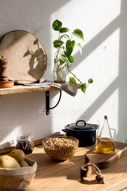 Различные ингредиенты и посуда, размещенные на деревянном столе во время приготовления пищи в домашней кухне с белой стеной и минималистичный интерьер в натуральном экологически чистом стиле — стоковое фото