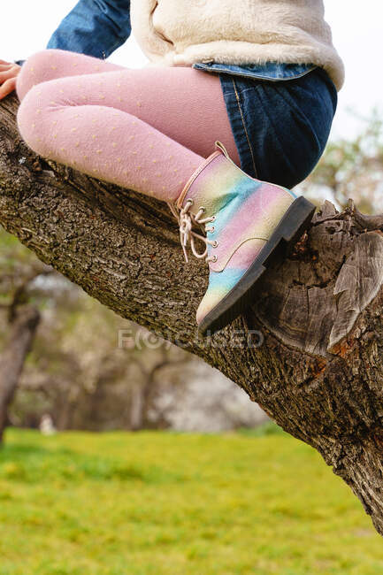 Crop bambino con gambe incrociate seduto sul tronco d'albero — Foto stock