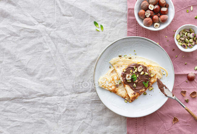 Vista superior de deliciosas crepes adornadas con chocolate y nueces servidas en el plato en la mesa para el desayuno - foto de stock