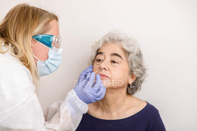 Mujer que realiza una prueba de PCR nasal en un paciente - foto de stock