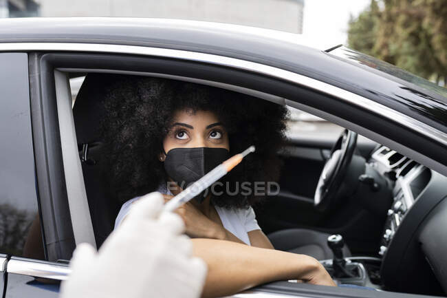 Enfermera irreconocible recortada en guantes de látex y uniforme vacunando a una paciente afroamericana dentro del automóvil en un viaje a través de una clínica móvil durante el brote de coronavirus - foto de stock