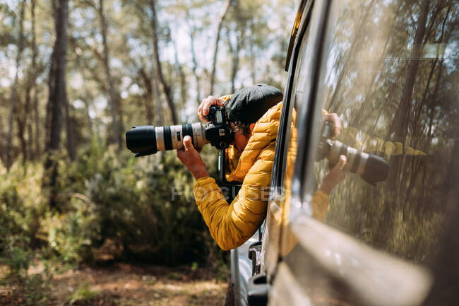 Vista laterale di un fotografo avventuroso che scatta foto dall'interno della sua auto fuoristrada — Foto stock