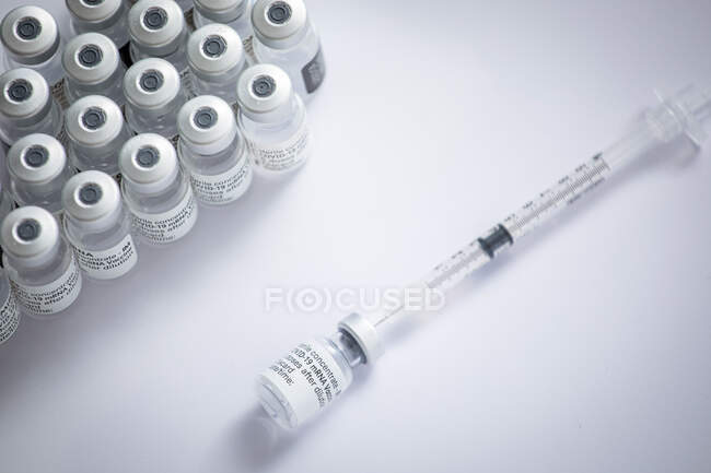 Acercamiento de algunos viales con la vacuna contra el coronavirus junto con una aguja sobre un fondo blanco - foto de stock