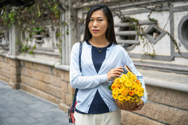 Belle asiatique fille portrait tandis qu'elle porte un panier en osier avec des fleurs jaunes. — Photo de stock