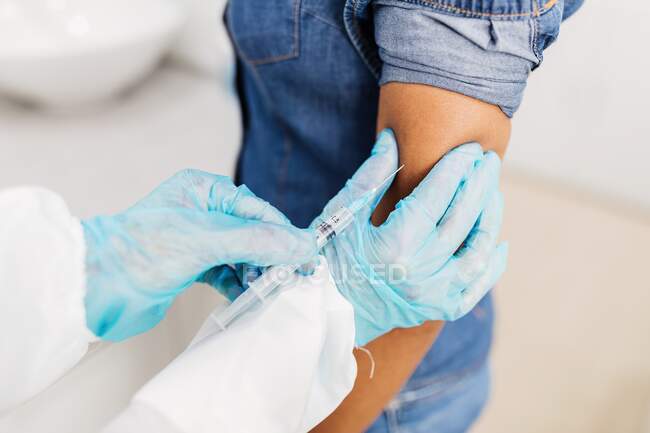 Шматок нерозпізнаного чоловіка - медика - захисника уніформи та латексних рукавичок, що вакцинують афроамериканського пацієнта в клініці під час спалаху коронавірусу. — стокове фото