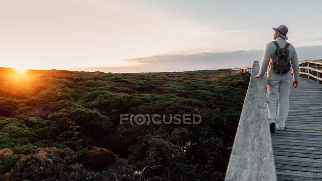 Uomo con zaino e cappello che cammina su una passerella guardando l'orizzonte — Foto stock