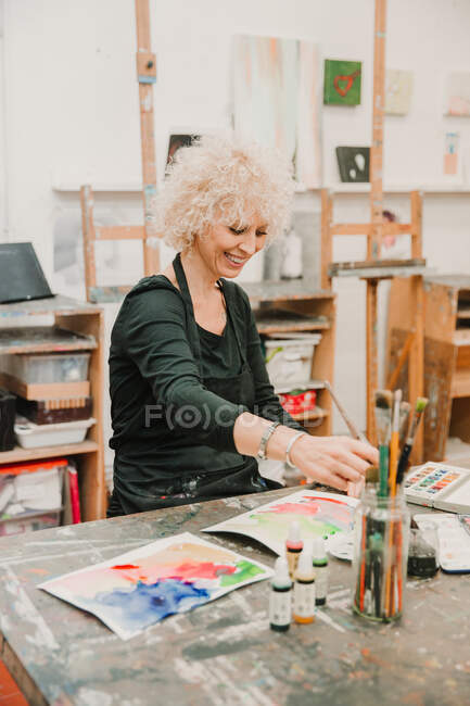 Artiste féminine concentrée assise à table et peignant à l'aquarelle sur papier tout en travaillant dans un atelier créatif — Photo de stock
