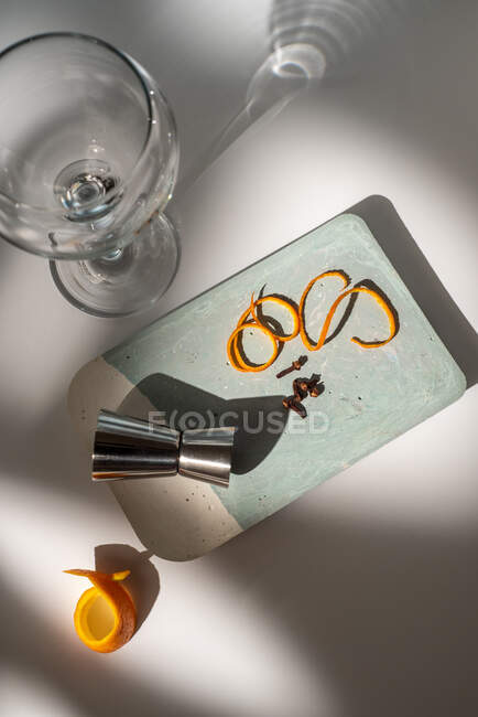 De cima de vidro perto de jigger metálico com raspas de frutas cítricas e condimentos secos na mesa com sombras — Fotografia de Stock
