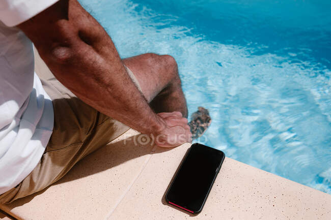 Вище врожаю нерозпізнаний чоловік-фрілансер сидить на подвір'ї біля смартфона з чорним екраном під час віддаленої роботи влітку. — стокове фото