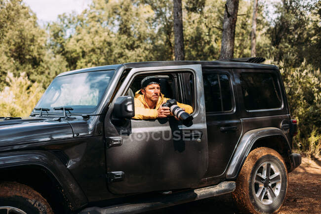 Side view of an adventurous photographer taking photos from inside his off-road car — Stock Photo