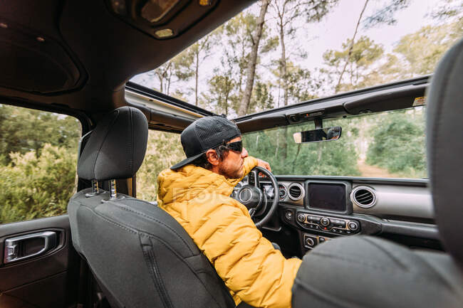 From behind inside view of a driver wearing a cap and sunglasses in an off-road car looking away — Stock Photo